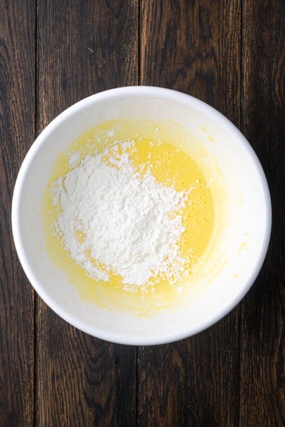 This banana cream pie recipe is a classic dessert with a rich vanilla custard layered with heaps of whipped cream and sweet banana slices. Cornstarch added to egg mixture in a bowl.