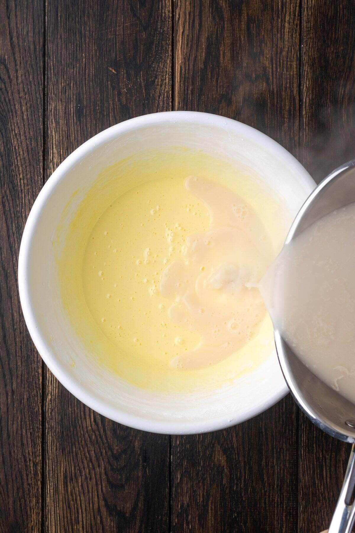 Pouring the custard mixture into a bowl of egg mixture to temper it.