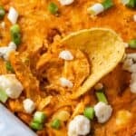 Close up of a chip stuck into buffalo chicken wing dip in a baking dish.