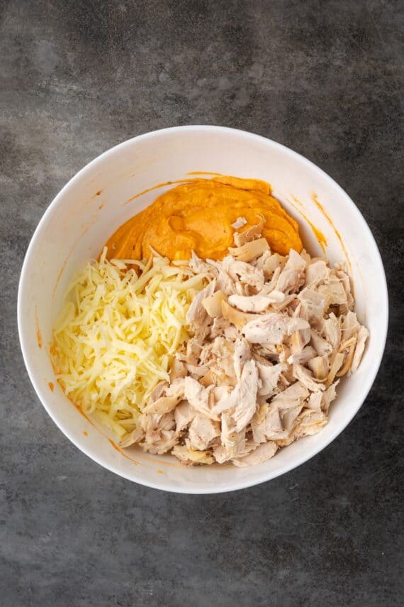 Chicken and shredded cheese added to a bowl of buffalo dip ingredients.