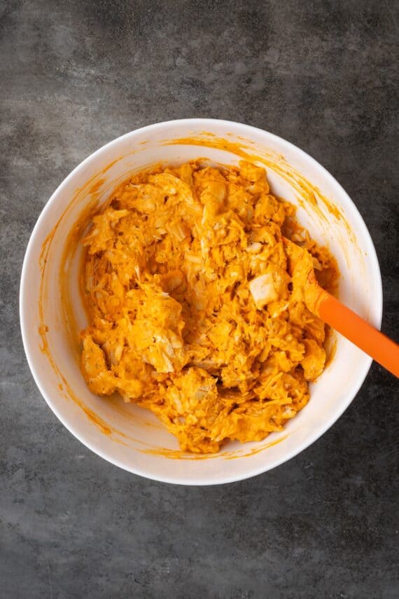 Chicken wing dip ingredients combined in a bowl with a red rubber spatula.