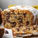 Glazed chocolate chip zucchini bread with a slice cut from the end on a wooden cutting board.