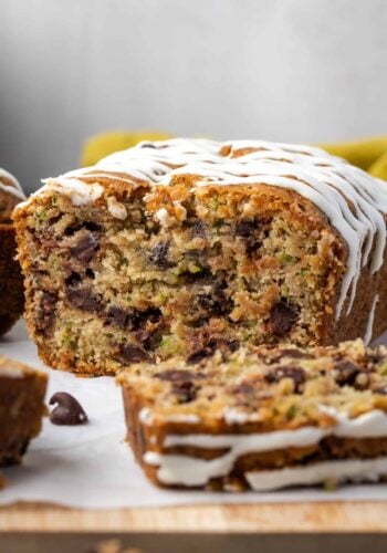 Glazed chocolate chip zucchini bread with a slice cut from the end on a wooden cutting board.