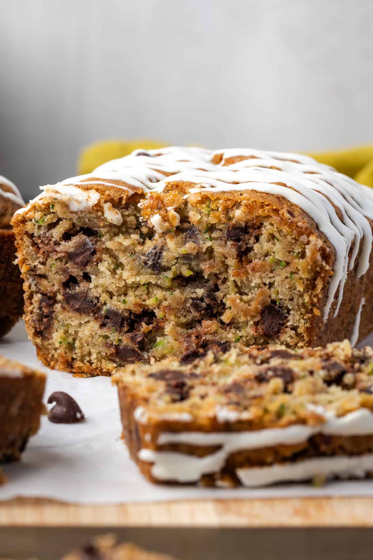 Glazed chocolate chip zucchini bread with a slice cut from the end on a wooden cutting board.