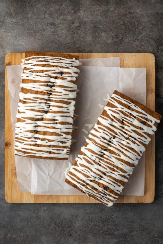 Overhead view of two chocolate chip zucchini bread loaves drizzled with glaze on a wooden cutting board.
