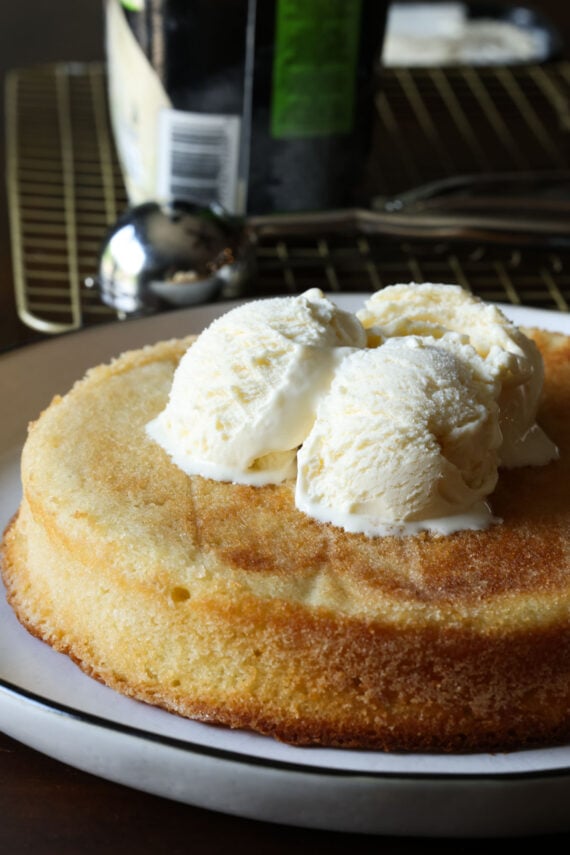 A large single layer butter cake topped with vanilla ice cream on a white plate
