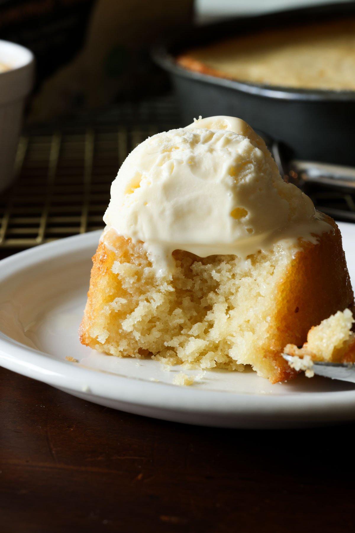 This insanely moist Copycat Butter Cake Recipe is a dupe for the Crumbl Butter Cake and the warm butter cake at California Pizza Kitchen. An individual butter cake on a white plate topped with vanilla ice cream and a bite taken out showing the tender inside