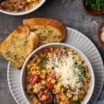 Overhead view of creamy Italian sausage soup in a bowl with a spoon, garnished with grated parmesan cheese, next to slices of garlic bread on a plate.