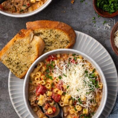 Overhead view of creamy Italian sausage soup in a bowl with a spoon, garnished with grated parmesan cheese, next to slices of garlic bread on a plate.