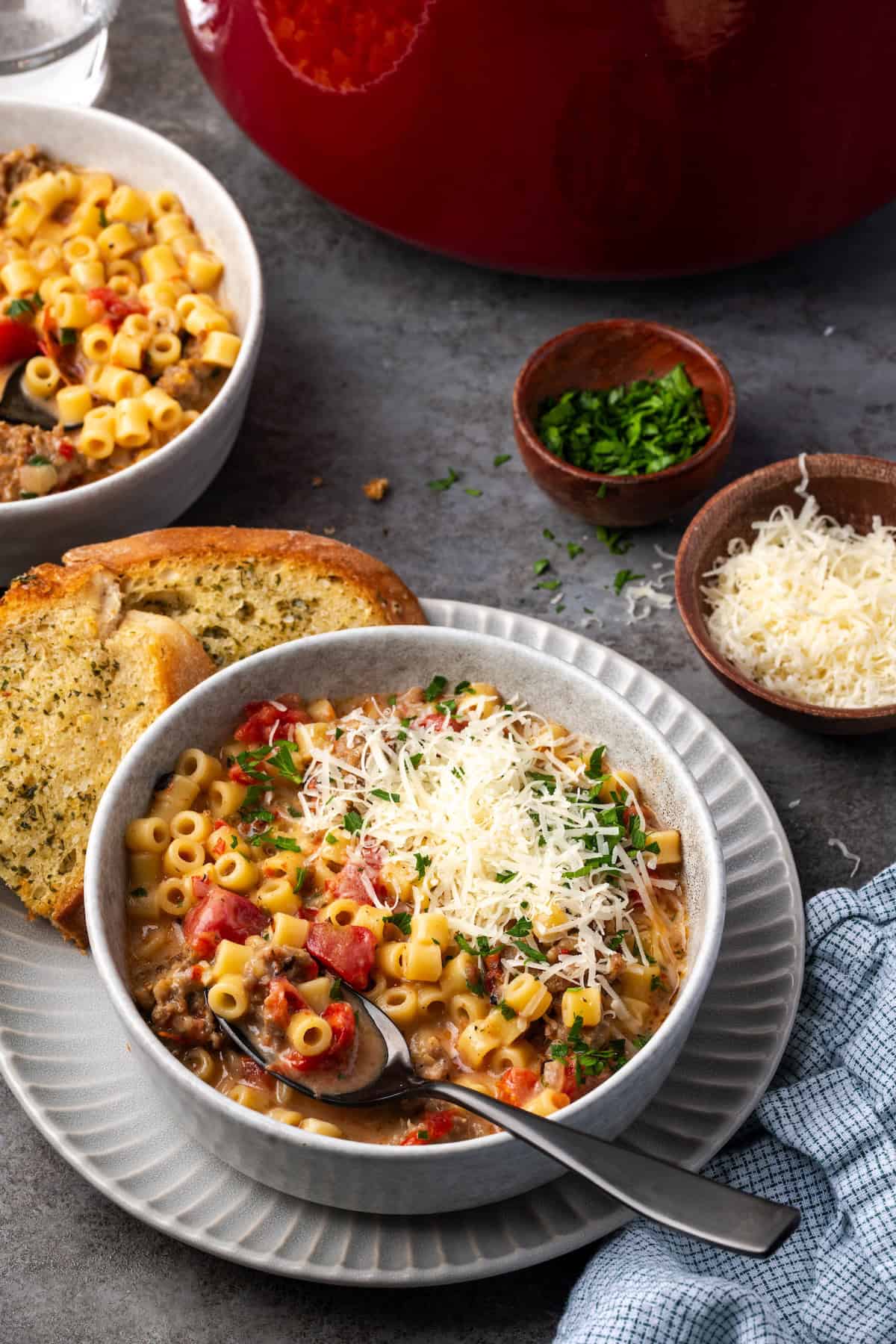 Creamy Italian sausage soup garnished with grated parmesan cheese in a bowl with a spoon, next to slices of garlic bread on a plate.