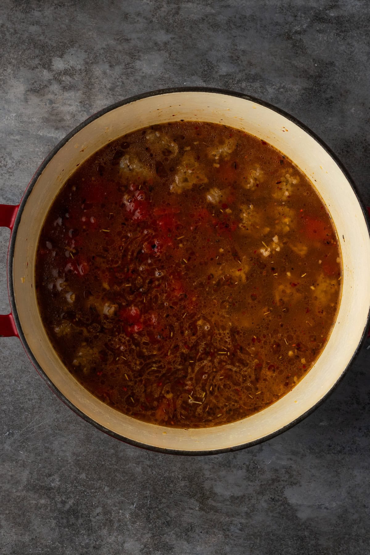 Broth and tomatoes added to browned sausage and onions in a pot.