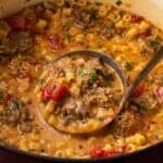 A ladle scooping creamy Italian sausage soup from a Dutch oven.