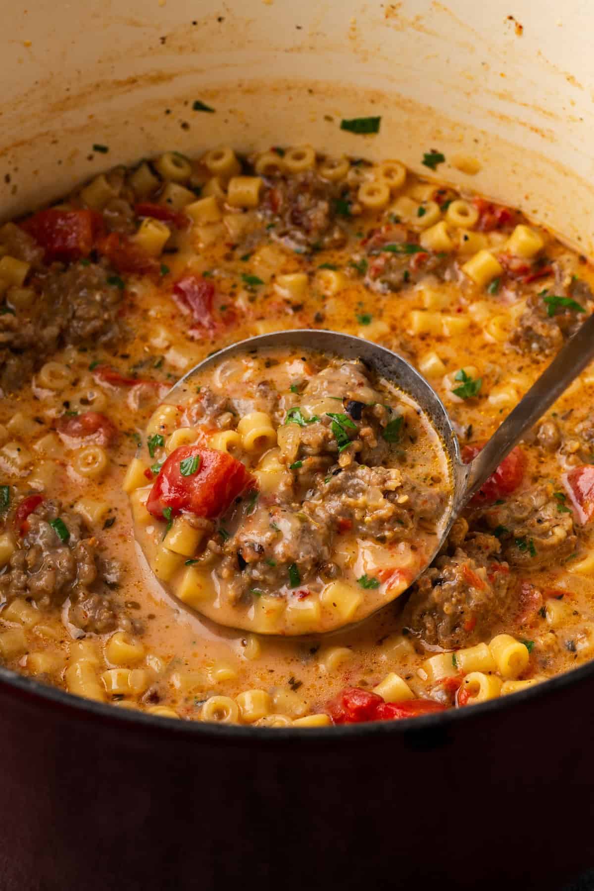 A ladle scooping creamy Italian sausage soup from a Dutch oven.