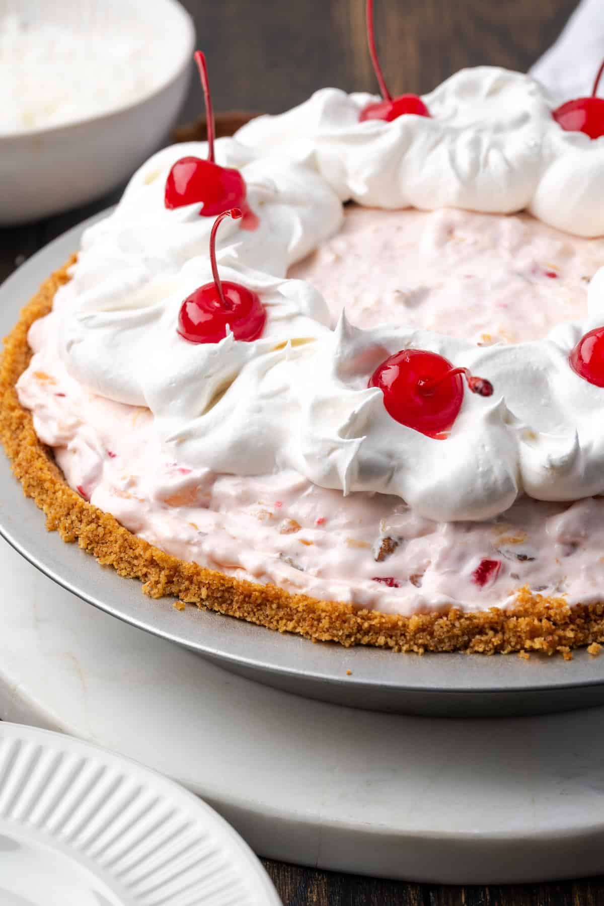 Millionaire pie is a decadent and fruity no-bake pie filled with sweet crushed pineapple, maraschino cherries, crispy pecans, and coconut. Millionaire pie decorated with swirls of whipped cream and whole maraschino cherries.