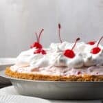 Side view of millionaire pie decorated with swirls of whipped cream and whole maraschino cherries.