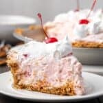 A slice of millionaire pie topped with whipped cream and a cherry on a plate, with the rest of the pie in the background.