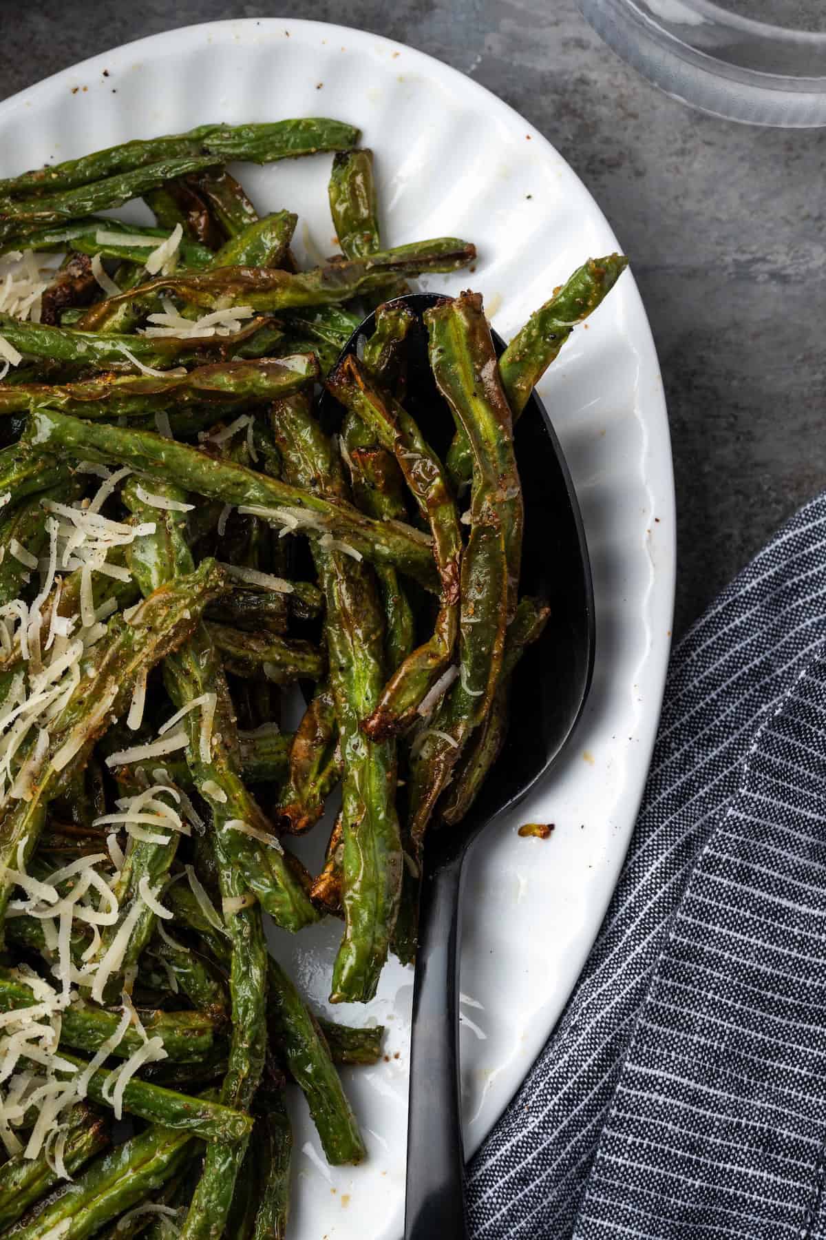 Overhead view of air fryer green beans topped with parmesan next to a serving spoon on a platter.