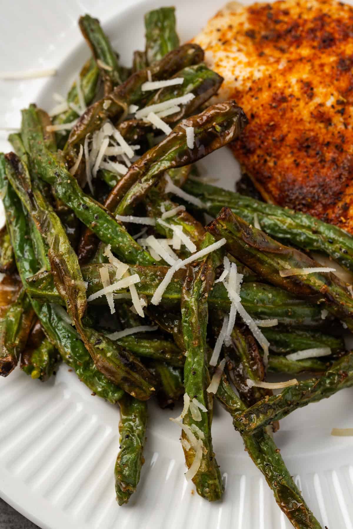 Close up of air fryer green beans served beside a baked chicken breast on a plate.
