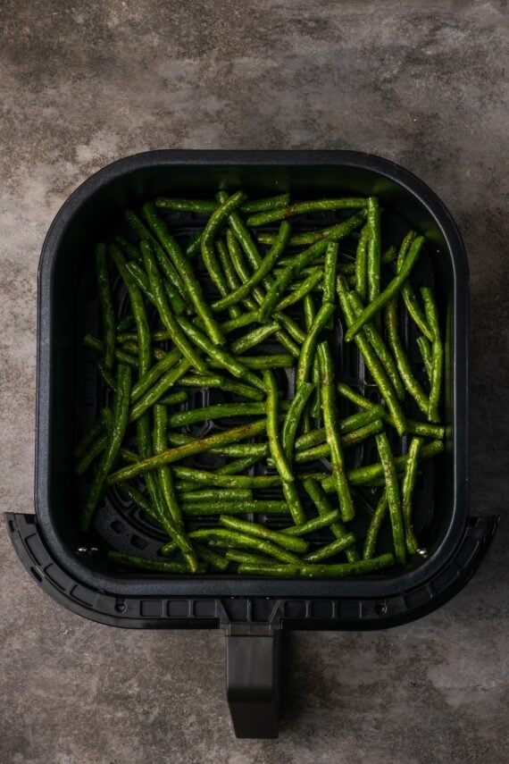 Seasoned green beans inside the air fryer basket.