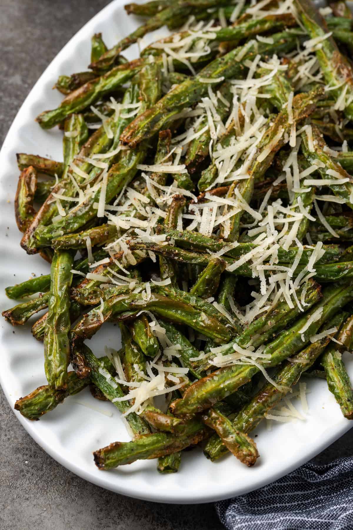 Air fryer green beans topped with parmesan cheese on a large platter.