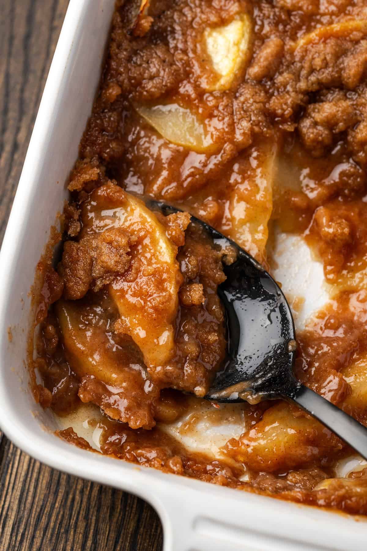 Close up overhead view of a spoon resting in the corner of apple brown betty in a baking dish.