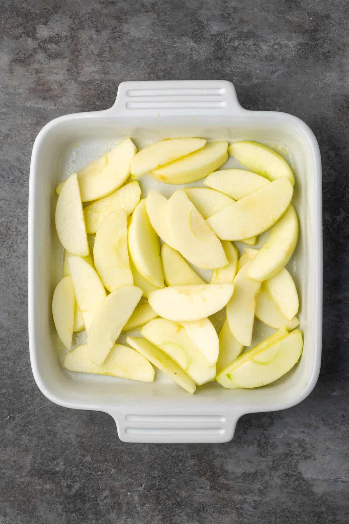 This easy apple brown betty is an old-fashioned dessert recipe with gooey baked apples layered with a buttery, sweet cinnamon crumble. Apple slices in the bottom of a baking dish.