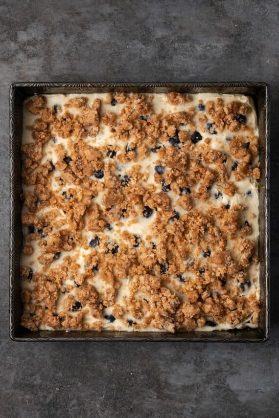 Overhead view of blueberry cake batter topped with crumble in a baking pan.