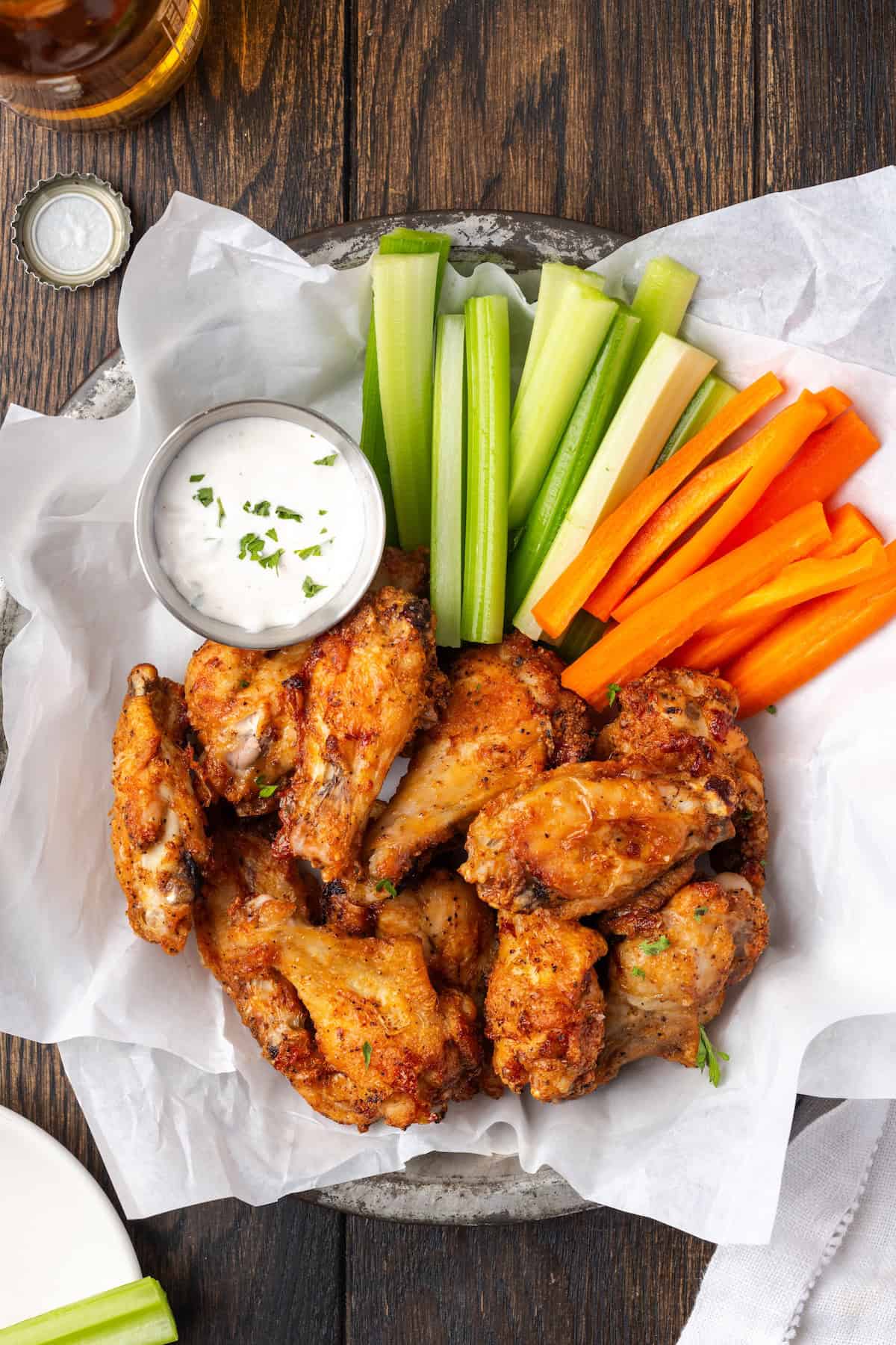 Overhead view of air fryer chicken wings in a serving basket with crudités and a side of ranch dressing.