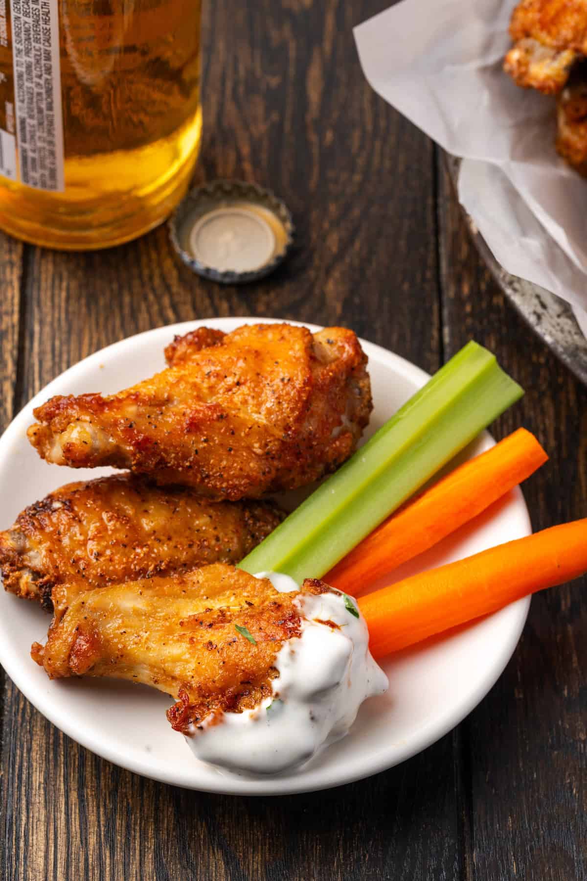 Three chicken wings with a side of crudités and dip on a plate.