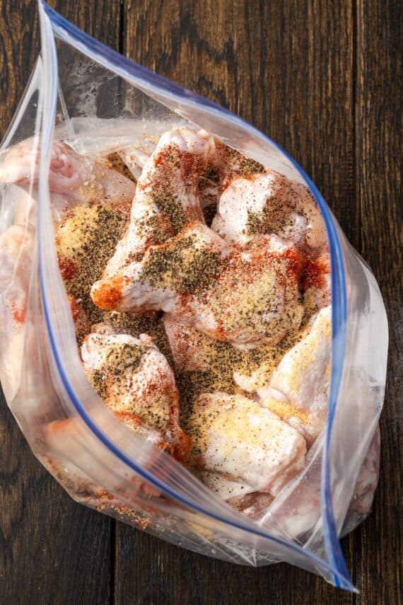 Seasonings added to raw chicken wings inside a large ziplock freezer bag.