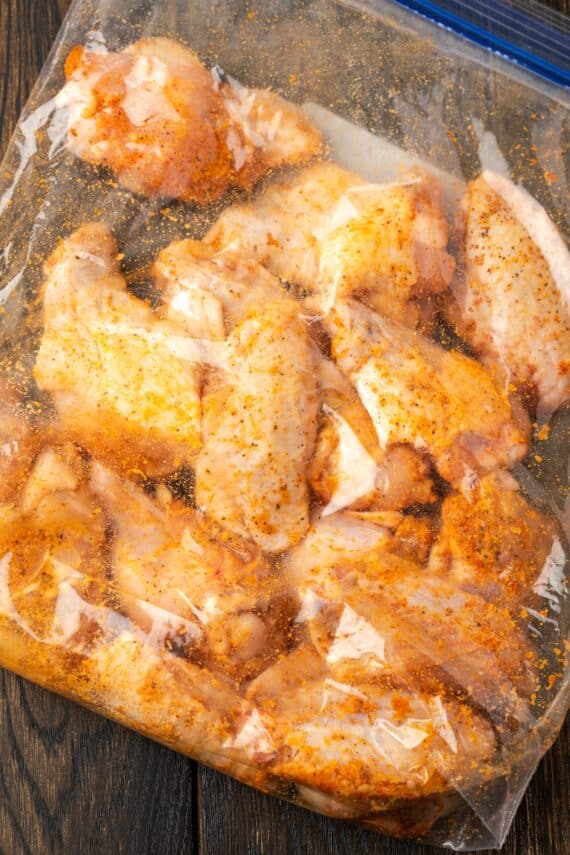 Seasoned raw chicken wings inside a large ziplock freezer bag.