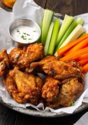 Air fryer chicken wings in a serving basket with crudités and a side of ranch dressing.