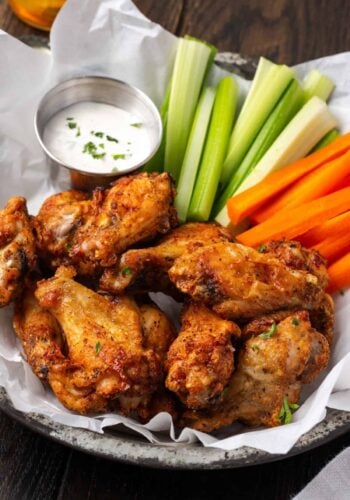 Air fryer chicken wings in a serving basket with crudités and a side of ranch dressing.