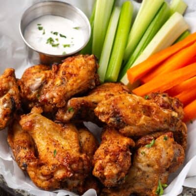 Air fryer chicken wings in a serving basket with crudités and a side of ranch dressing.
