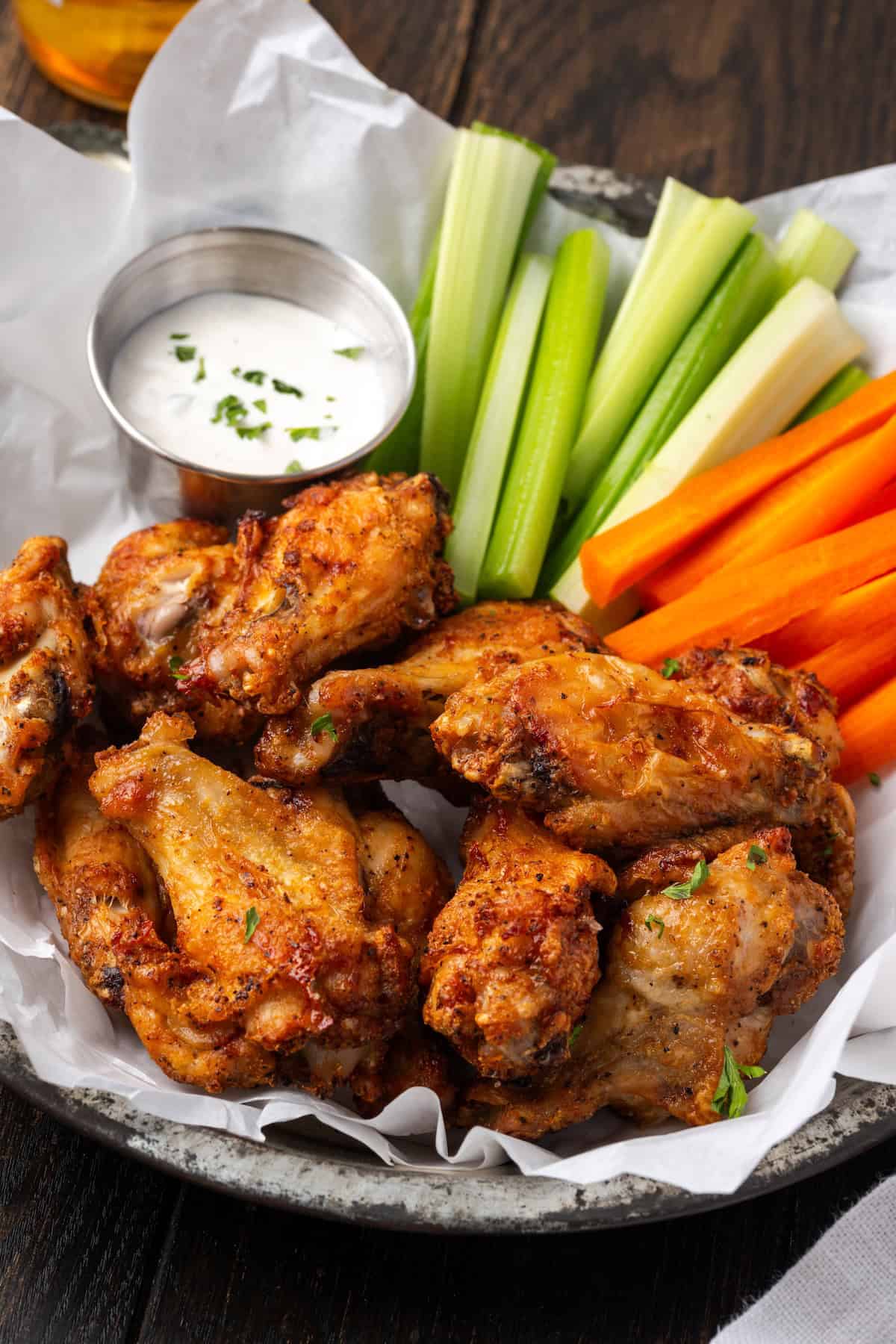 Air fryer chicken wings in a serving basket with crudités and a side of ranch dressing.