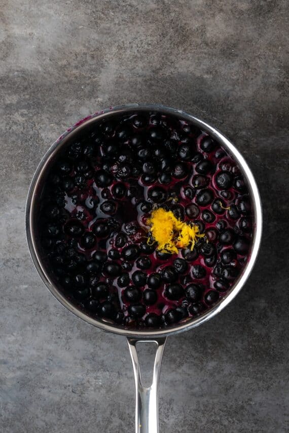Lemon zest added to blueberry sauce in a saucepan.