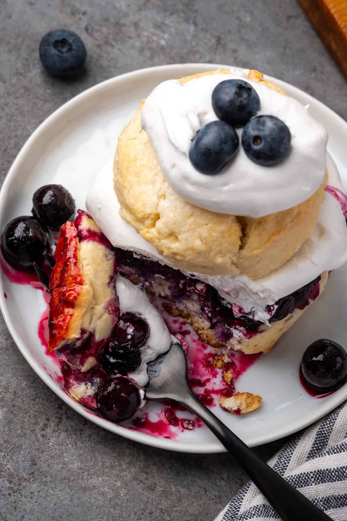 Overhead view of a forkful resting next to blueberry shortcake on a plate.