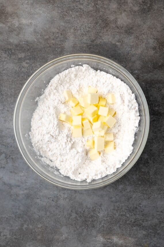 Cubed butter added to dry ingredients in a bowl.
