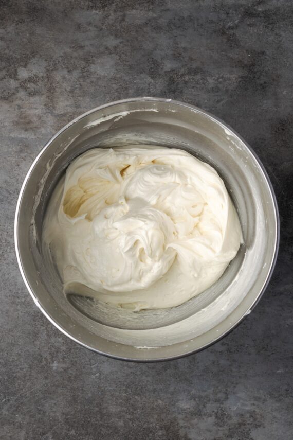 This red velvet cheesecake has four decadent layers of creamy cheesecake and soft red velvet cake smothered with cream cheese frosting. Cream cheese frosting in a mixing bowl.