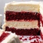 Side view of a red velvet cheesecake with a large slice missing, revealing the cake and cheesecake layers.
