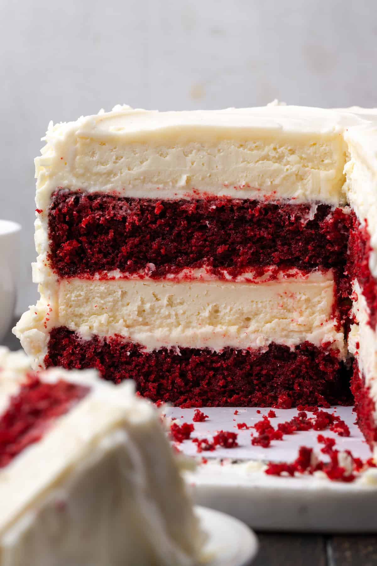 This red velvet cheesecake has four decadent layers of creamy cheesecake and soft red velvet cake smothered with cream cheese frosting. Side view of a red velvet cheesecake with a large slice missing, revealing the cake and cheesecake layers.
