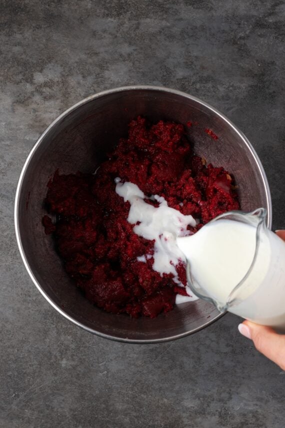 This red velvet cheesecake has four decadent layers of creamy cheesecake and soft red velvet cake smothered with cream cheese frosting. Buttermilk added to red velvet cake batter in a bowl.