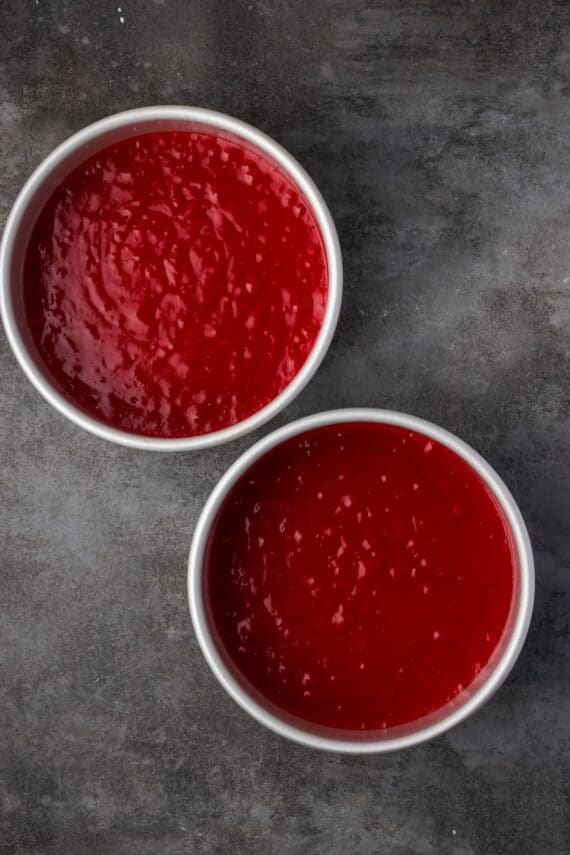 This red velvet cheesecake has four decadent layers of creamy cheesecake and soft red velvet cake smothered with cream cheese frosting. Two round pans filled with red velvet cake batter.