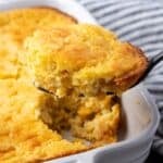 Spoon bread in a baking dish with a spoon scooping from the corner.