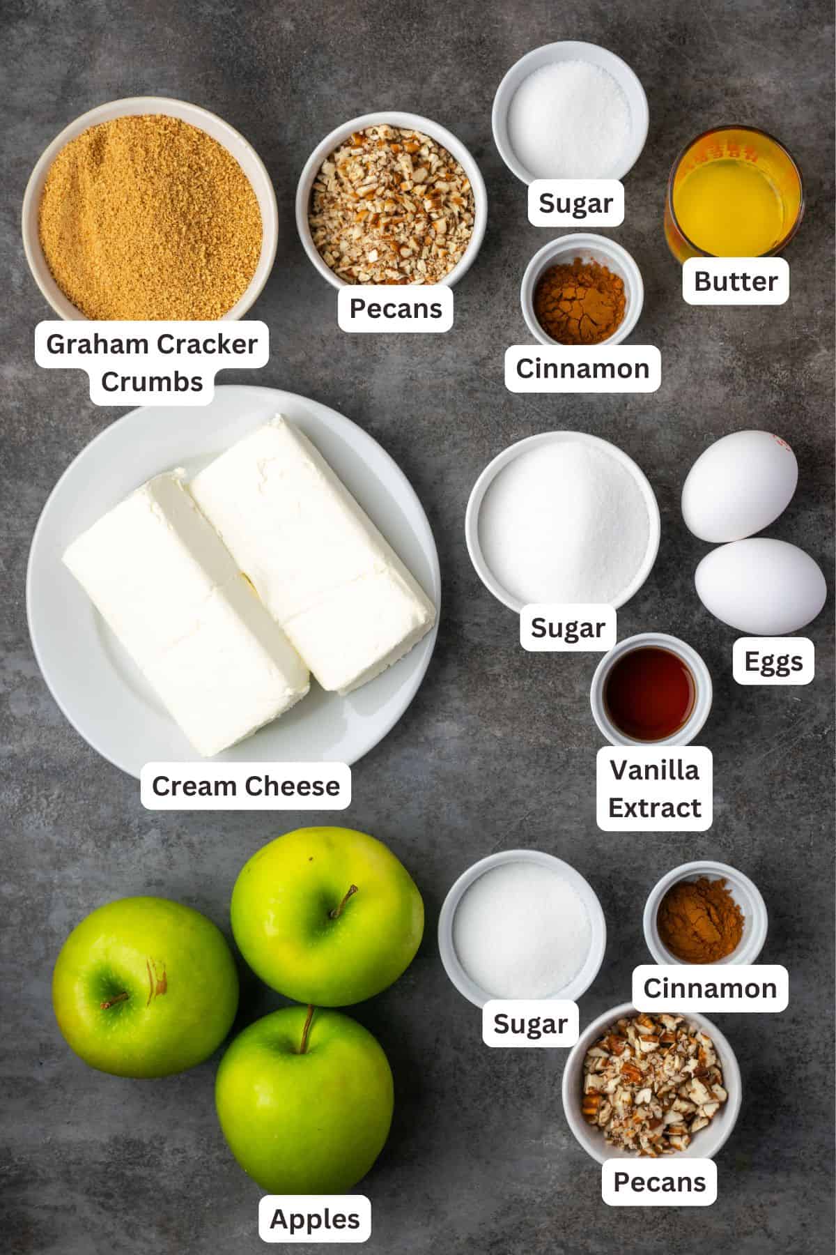 This homemade apple cheesecake recipe has a buttery graham cracker crust layered with creamy cheesecake and a gooey caramel apple topping. Apple cheesecake ingredients with text labels overlaying each ingredient.