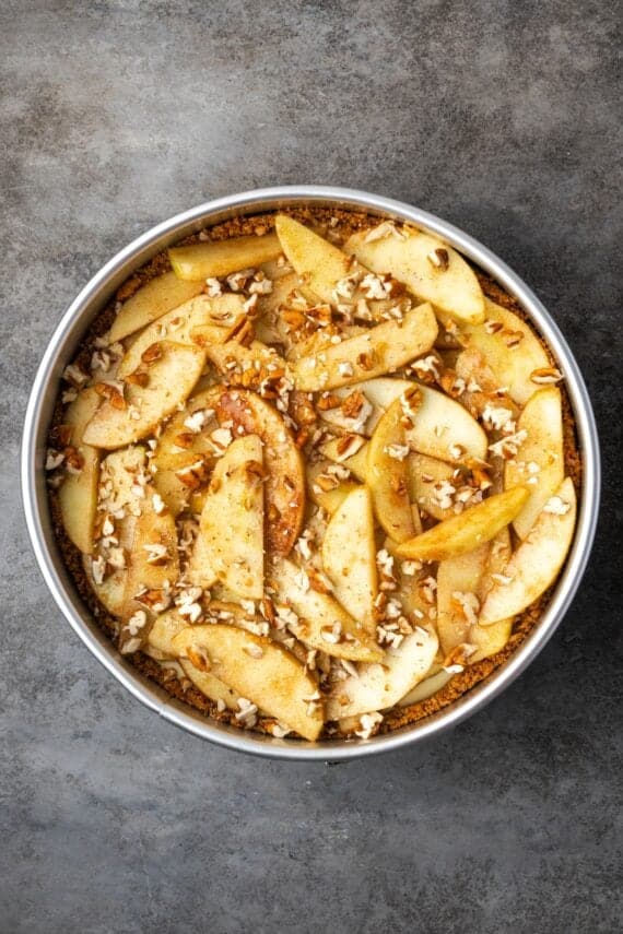 This homemade apple cheesecake recipe has a buttery graham cracker crust layered with creamy cheesecake and a gooey caramel apple topping. Cheesecake topped with cinnamon apples and pecans in a springform pan.