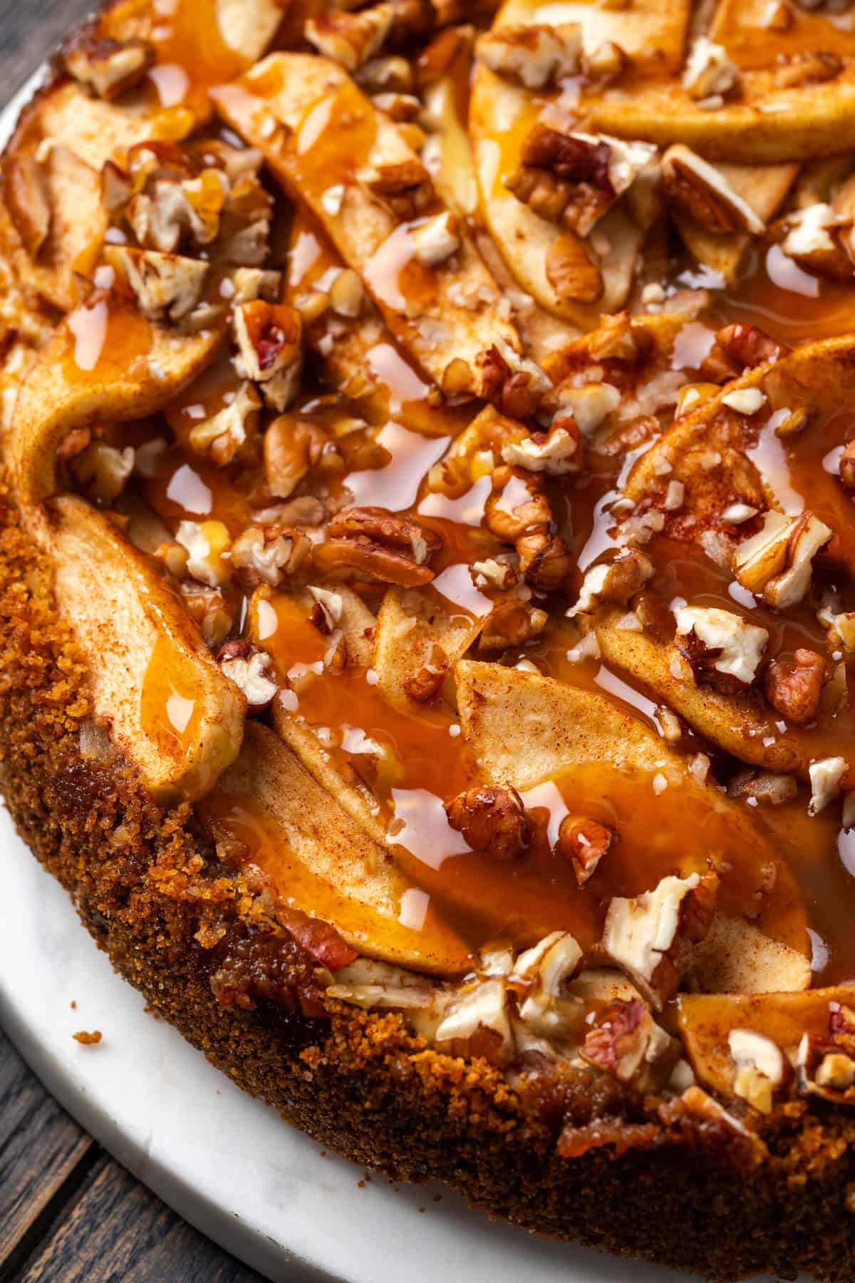 This homemade apple cheesecake recipe has a buttery graham cracker crust layered with creamy cheesecake and a gooey caramel apple topping. Close up of an apple cheesecake covered with caramel and chopped pecans.