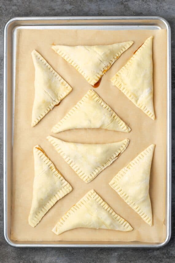 Crispy, buttery store-bought puff pastry and quick, homemade apple filling make these easy apple turnovers the perfect fall weekend treat! Overhead view of folded puff pastry apple turnovers on a baking sheet.