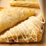 Apple turnovers a baking sheet, with one turnover topped with icing.