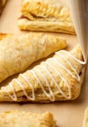 Apple turnovers a baking sheet, with one turnover topped with icing.